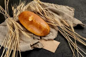 Wheat bread loaf on coarse burlap with ears of wheat on black background photo