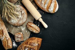 Top view of baguette, baked bread, flour and wheat spikes composition with wheat flour sprinkled around on a dark background photo