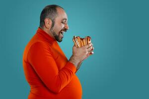 Close-up portrait of a middle-aged man with beard, dressed in a red turtleneck, posing with burgers against a blue background. Fast food. photo