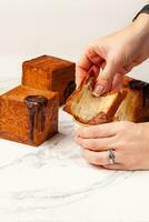 Woman hands dipping slice of cube shaped croissant into creamy chocolate custard photo