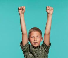 Close-up portrait of a blonde teenage boy in a green shirt with palm print posing against a blue studio background. Concept of sincere emotions. photo