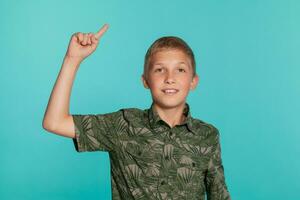 Close-up portrait of a blonde teenage boy in a green shirt with palm print posing against a blue studio background. Concept of sincere emotions. photo