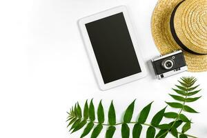 Straw hat with green leaves, tablet and old camera on white background, Summer background. Top view photo