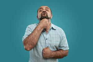 Close-up portrait of a brunet middle-aged man with beard, dressed in a light checkered shirt and posing against a blue background. photo