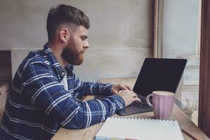 joven hombre chateando vía netbook durante trabajo descanso en café tienda foto