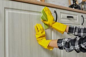 Hands in gloves with green rag is cleaning kitchen cabinets - housework and housekeeping concept photo