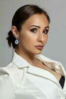 Close up portrait of a brunette model girl with professional evening make-up, wearing a white jacket with black bra, posing on gray background. photo