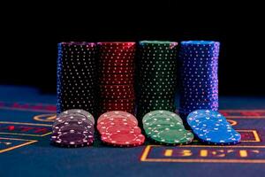 Colorful chips nicely laid out near piles on blue cover of playing table. Black background. Gambling entertainment, poker, casino concept. Close-up. photo