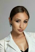 Close up portrait of a brunette model girl with professional evening make-up, wearing a white jacket with black bra, posing on gray background. photo