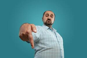 Close-up portrait of a brunet middle-aged man with beard, dressed in a light checkered shirt and posing against a blue background. photo