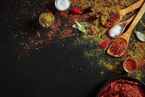 Assorted spices on dark black background. Seasonings for food. Curry, paprika, pepper, cardamom, turmeric. Top view. photo