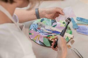 Workplace of the mosaic master women's hands holding tool for mosaic details in the process of making a mosaic photo