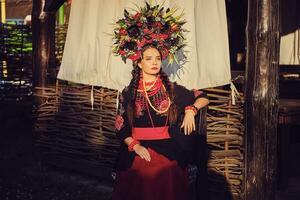 morena niña en un negro y rojo bordado ucranio auténtico nacional disfraz y un guirnalda de flores es posando en contra un terraza. de cerca. foto