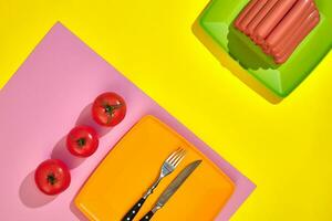 Stack of thin wiener sausages with tomatoes on plate on pink and yellow background photo