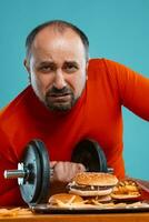 de cerca retrato de un de edad mediana hombre con barba, vestido en un rojo suéter tipo con cuello de tortuga, posando con hamburguesas y francés papas fritas azul antecedentes. rápido alimento. foto