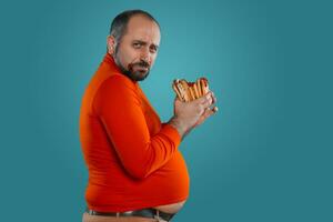 Close-up portrait of a middle-aged man with beard, dressed in a red turtleneck, posing with burgers against a blue background. Fast food. photo