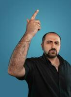 Close-up portrait of a brunet middle-aged man with beard, dressed in a black t-shirt and posing against a blue background. photo