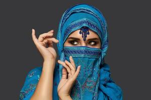 Studio shot of a young beautiful woman wearing the blue hijab decorated with sequins and jewelry. Arabic style. photo