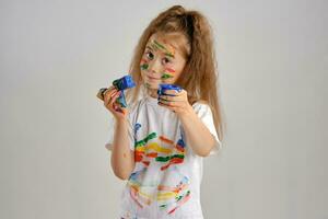 Little girl in white painted t-shirt, with colored face is playing with a sponge soaked in paint. Isolated on white. Close-up. photo