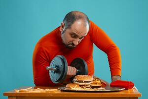 de cerca retrato de un de edad mediana hombre con barba, vestido en un rojo suéter tipo con cuello de tortuga, posando con hamburguesas y francés papas fritas azul antecedentes. rápido alimento. foto