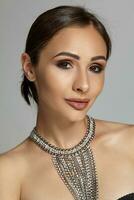 Close up portrait of a brunette model girl with professional evening make-up, wearing a black bra and necklace, posing on gray background. photo