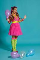 encantador niña con un multicolor trenzas peinado y brillante constituir, posando en estudio con aire globos en contra un azul antecedentes. foto