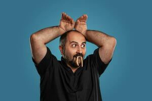 Close-up portrait of a brunet middle-aged man with beard, dressed in a black t-shirt and posing against a blue background. photo