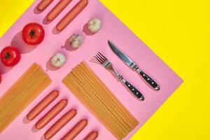 Sausages with tomatoes, spaghetti and garlic on a yellow and pink minimal background. Flat lay. Top view. photo