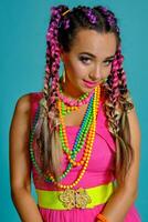 Lovely girl with a multi-colored braids hairstyle and bright make-up, posing in studio against a blue background. photo