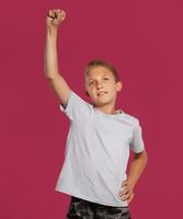 Close-up portrait of a blonde teenage boy in a white t-shirt posing against a pink studio background. Concept of sincere emotions. photo