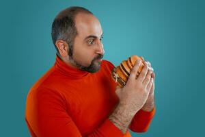 de cerca retrato de un de edad mediana hombre con barba, vestido en un rojo suéter tipo con cuello de tortuga, posando con hamburguesas en contra un azul antecedentes. rápido alimento. foto