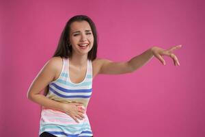 Brunette woman with long hair, dressed in colorful striped shirt, posing against pink studio background. Sincere emotions. Close-up. photo