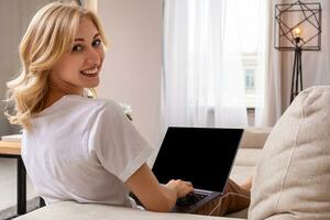 Woman on sofa working on laptop with mockup blank screen. Empty copy space on monitor for advertisement. Black screen. photo