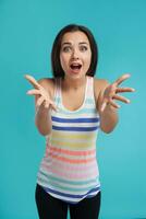 Brunette woman with long hair, dressed in striped shirt and black leggings, posing against blue studio background. Sincere emotions. Close-up. photo