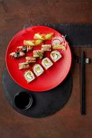 Sushi rolls with eel, cream cheese and orange pulp served on red plate with nigirizushi with eel, unagi sauce and sesame and salmon topped with avocado and caviar. Traditional Japanese cuisine photo