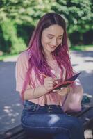 mujer escritura en un cuaderno sentado en un de madera banco en el par foto