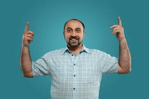 Close-up portrait of a brunet middle-aged man with beard, dressed in a light checkered shirt and posing against a blue background. photo