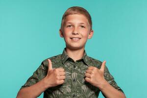 Close-up portrait of a blonde teenage boy in a green shirt with palm print posing against a blue studio background. Concept of sincere emotions. photo