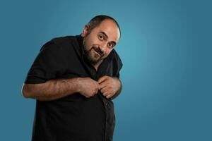 Close-up portrait of a brunet middle-aged man with beard, dressed in a black t-shirt and posing against a blue background. photo