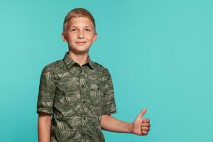 Close-up portrait of a blonde teenage boy in a green shirt with palm print posing against a blue studio background. Concept of sincere emotions. photo