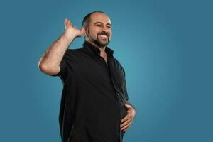 Close-up portrait of a brunet middle-aged man with beard, dressed in a black t-shirt and posing against a blue background. photo