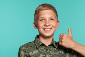 Close-up portrait of a blonde teenage boy in a green shirt with palm print posing against a blue studio background. Concept of sincere emotions. photo