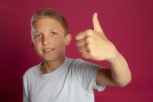 Close-up portrait of a blonde teenage boy in a white t-shirt posing against a pink studio background. Concept of sincere emotions. photo