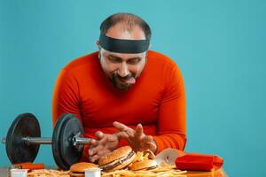 Middle-aged man with beard, dressed in a red turtleneck, headband, posing with burgers and french fries. Blue background. Close-up. Fast food. photo