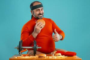 Middle-aged man with beard, dressed in a red turtleneck, headband, posing with burgers and french fries. Blue background. Close-up. Fast food. photo