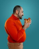 Close-up portrait of a middle-aged man with beard, dressed in a red turtleneck, posing with burgers against a blue background. Fast food. photo