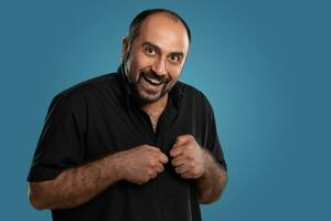 Close-up portrait of a brunet middle-aged man with beard, dressed in a black t-shirt and posing against a blue background. photo