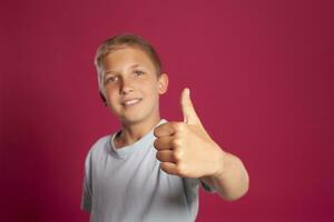 Close-up portrait of a blonde teenage boy in a white t-shirt posing against a pink studio background. Concept of sincere emotions. photo