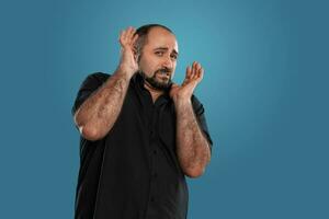 de cerca retrato de un moreno de edad mediana hombre con barba, vestido en un negro camiseta y posando en contra un azul antecedentes. foto