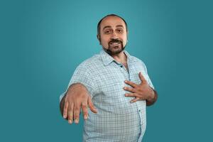 Close-up portrait of a brunet middle-aged man with beard, dressed in a light checkered shirt and posing against a blue background. photo